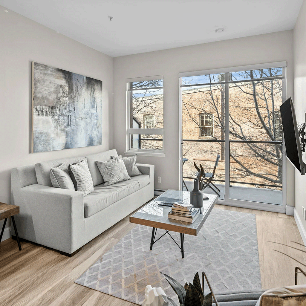 Stylish urban living room with a sleek grey sofa, minimalist decor, and large windows overlooking the city of Victoria.