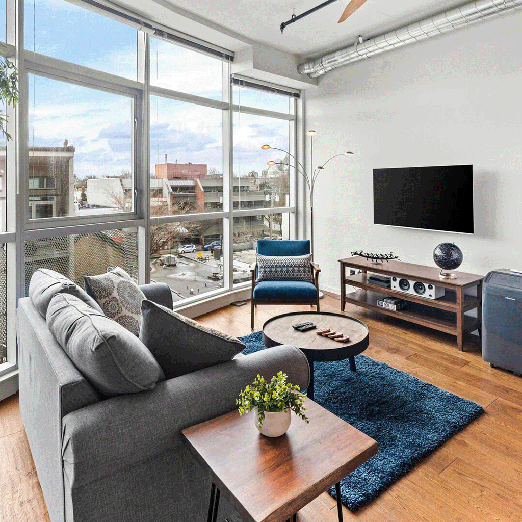 Loft-style living room with industrial design elements, high ceilings, and large urban-facing windows in Victoria