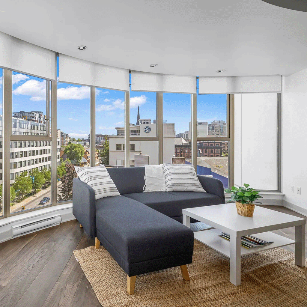 Spacious corner living area with panoramic city views through floor-to-ceiling windows, minimalist furniture and soft natural light