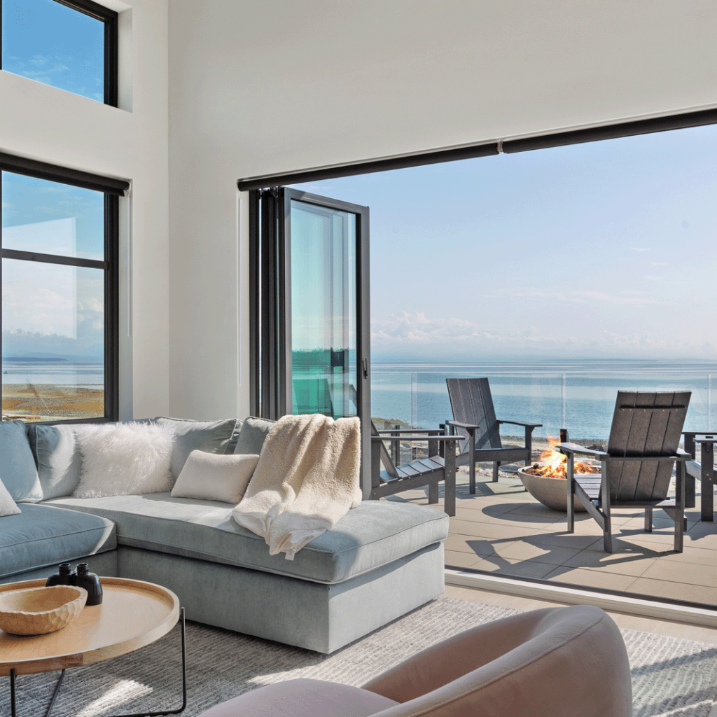 Expertly managed modern living room with expansive ocean views through large windows, featuring stylish furnishings and a welcoming fireplace.
