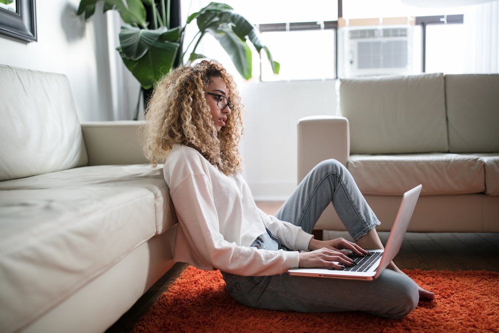 Young woman working from home on a laptop, sitting on the floor in a relaxed environment