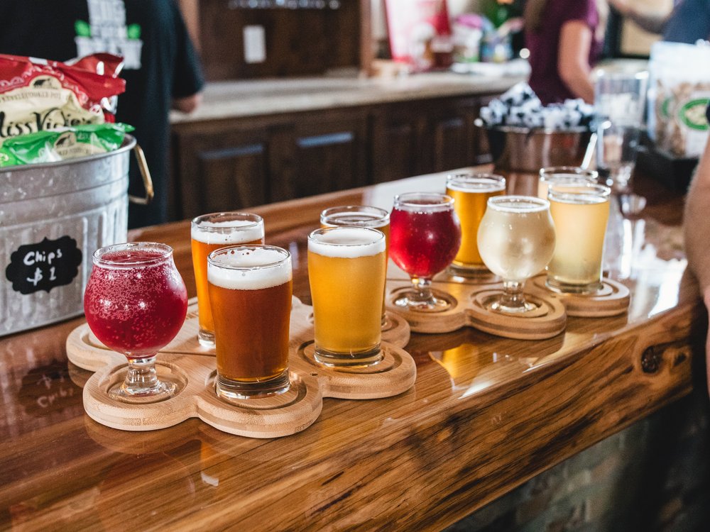 A selection of craft beers in various colors served in unique glasses on a wooden bar counter.