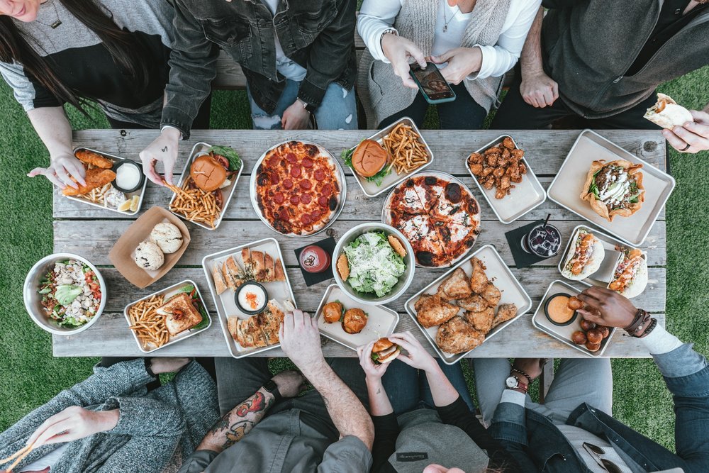 Group of friends enjoying an outdoor picnic with a variety of foods on a wooden table