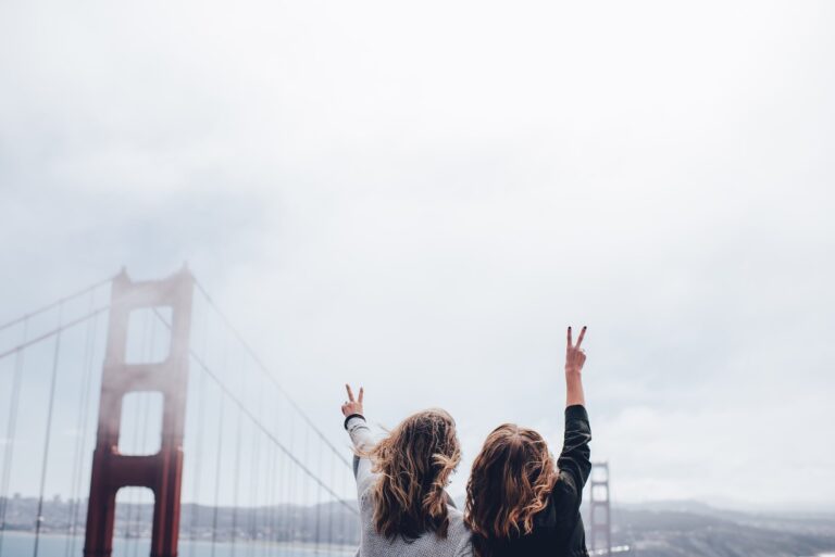 Two youths nurses extending their arms in victory in front of the Golden Gate Bridge on a cloudy day.